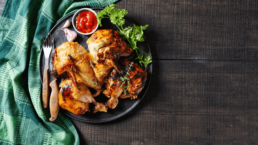 Chicken Lunch roast chicken on a plate with a pot of sauce knife and fork with green napkin